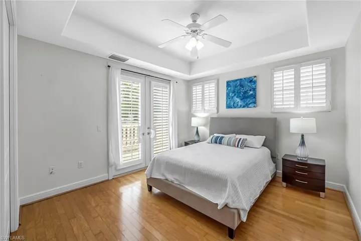 Bedroom with a tray ceiling, access to exterior, light wood-type flooring, and ceiling fan