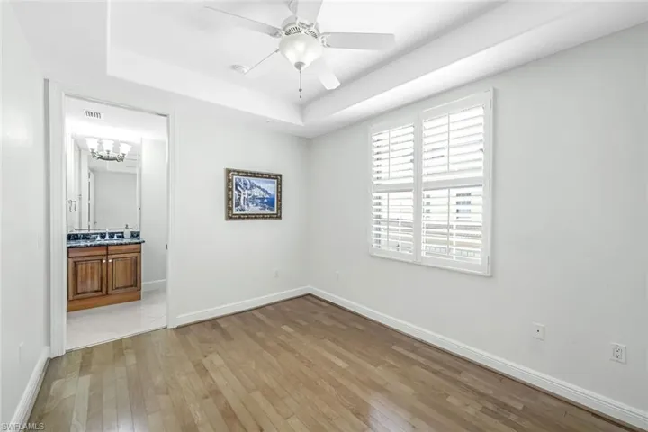 Unfurnished bedroom with light wood finished floors, a tray ceiling, connected bathroom, ceiling fan, and a chandelier