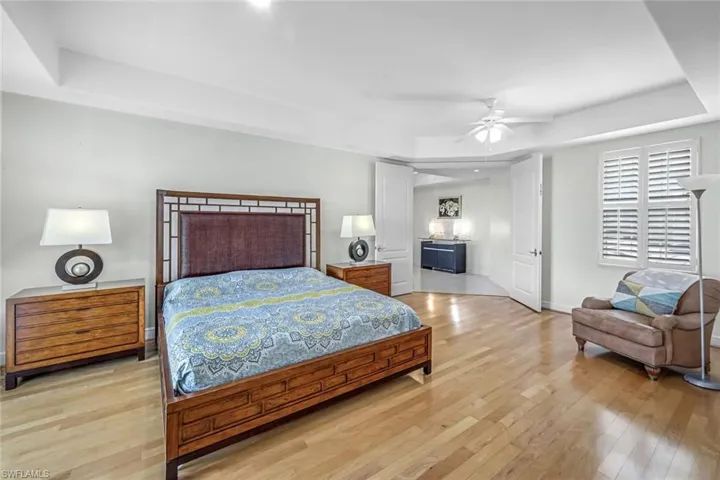 Bedroom with a raised ceiling, light wood-type flooring, and a ceiling fan
