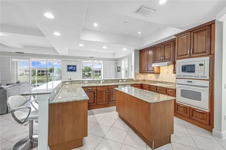 Kitchen featuring a peninsula, a tray ceiling, light stone countertops, white appliances, and open floor plan