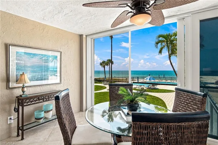Expansive sliding glass doors, textured wall finishes, ceiling fan with light fixture, tile flooring, and a glass-top table