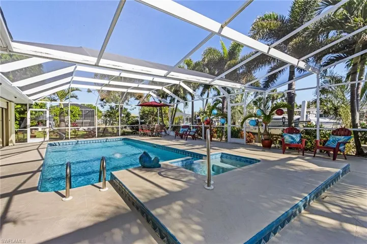 View of pool with an in ground hot tub, glass enclosure, and a patio area