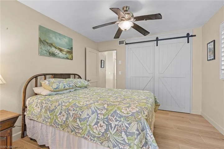Bedroom with light wood-type flooring, a barn door, a closet, and ceiling fan