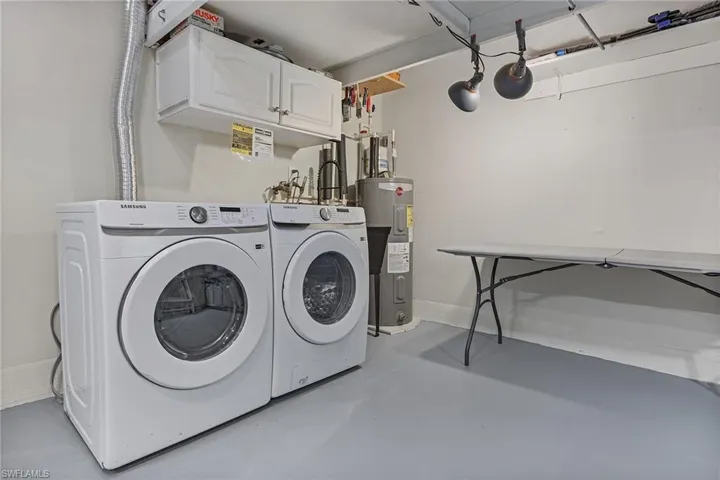 Clothes washing area featuring electric water heater, cabinets, and separate washer and dryer