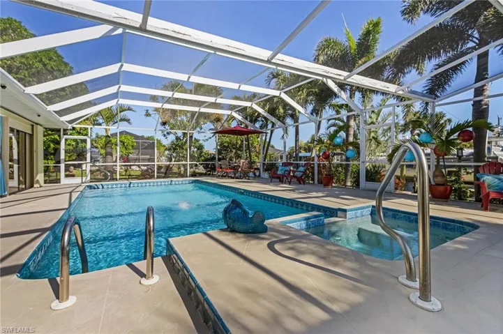 View of pool with glass enclosure, a patio area, and an in ground hot tub