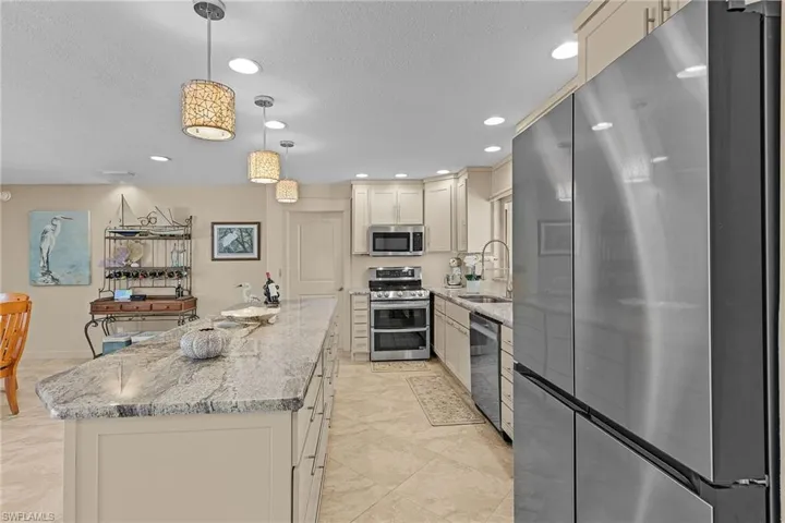 Kitchen featuring light stone countertops, appliances with stainless steel finishes, sink, a center island, and hanging light fixtures