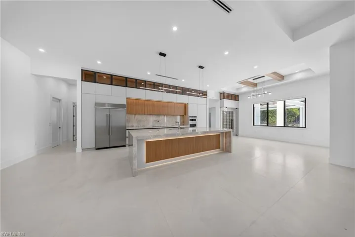 Dual tone kitchen with modern cabinets, light stone counters, open floor plan, a large island, and stainless steel built in fridge