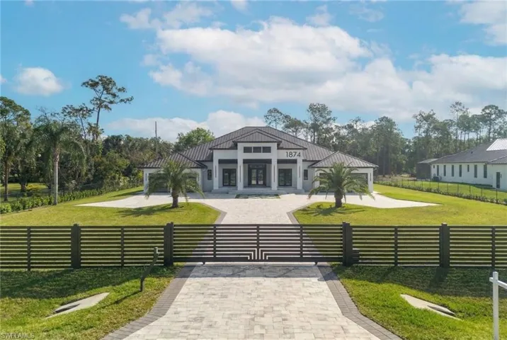 View of home's gate, a fenced front yard, a patio area, driveway, and view of wooded area