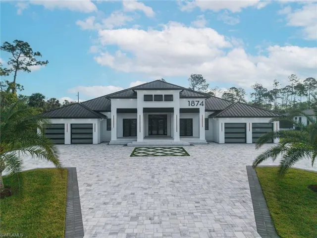 View of front of property featuring a garage, a standing seam roof, driveway, and stucco siding