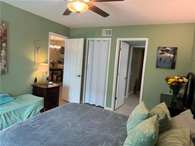 Bedroom featuring light tile patterned flooring, ensuite bathroom, and ceiling fan with notable chandelier