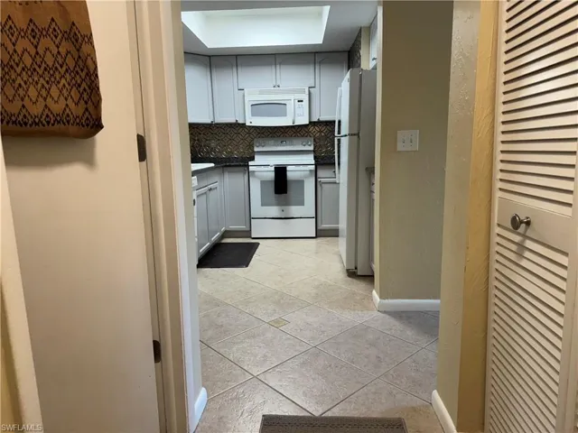 Kitchen featuring light tile patterned flooring, backsplash, and white appliances