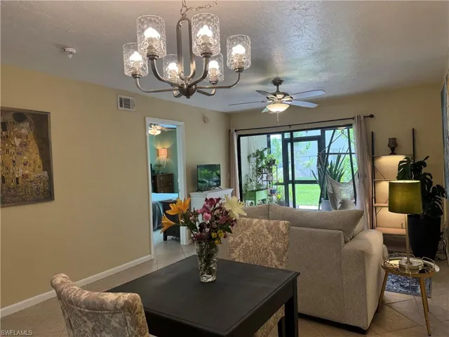 Tiled living room with a textured ceiling and ceiling fan with notable chandelier