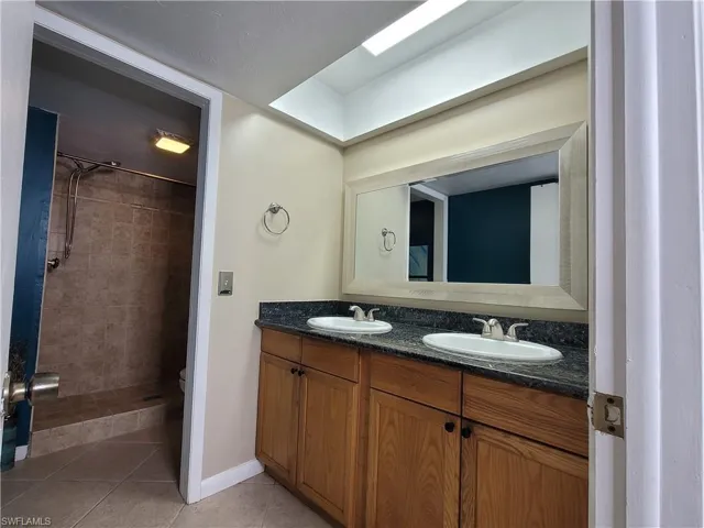 Bathroom with tiled shower, double vanity, and tile flooring