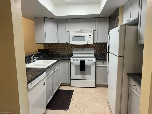 Kitchen featuring tasteful backsplash, white appliances, sink, light tile patterned floors, and gray cabinetry
