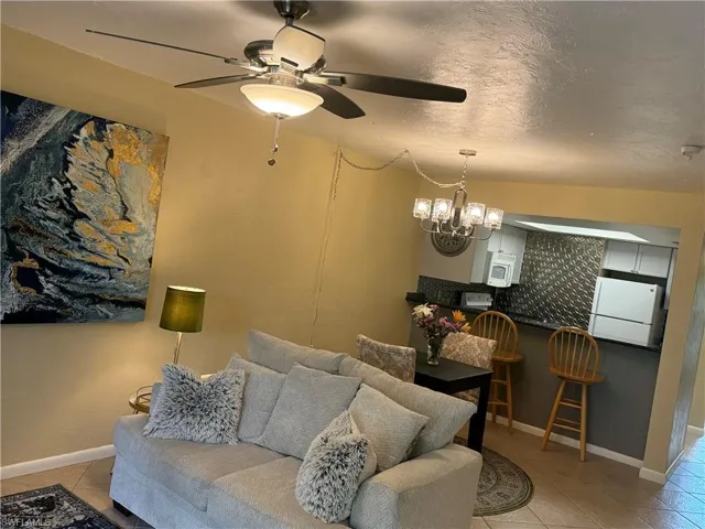 Living room with ceiling fan with notable chandelier and tile patterned floors