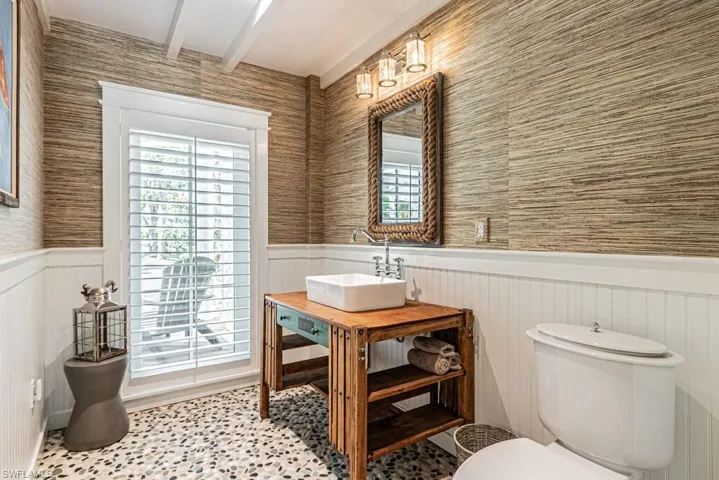 Half bathroom with a sink, a wainscoted wall, beam ceiling, plenty of natural light, and toilet
