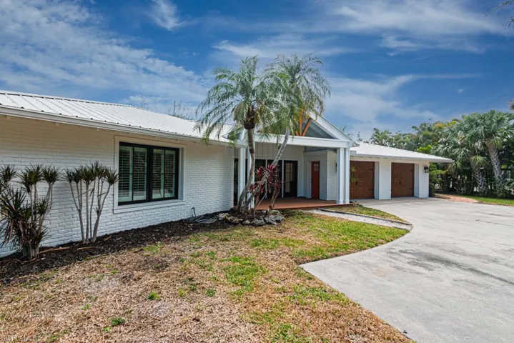 View of front facade with brick siding, driveway, an attached garage, metal roof, and a porch