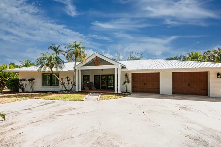 View of front of property featuring metal roof, driveway, brick siding, and an attached garage