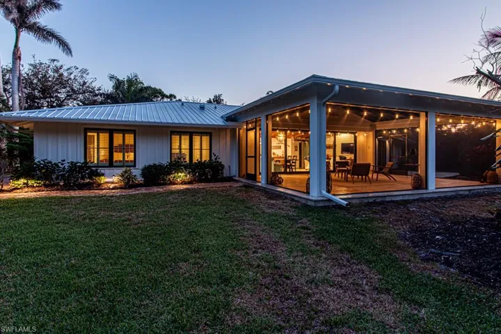 Rear view of house featuring a sunroom, a yard, board and batten siding, and metal roof