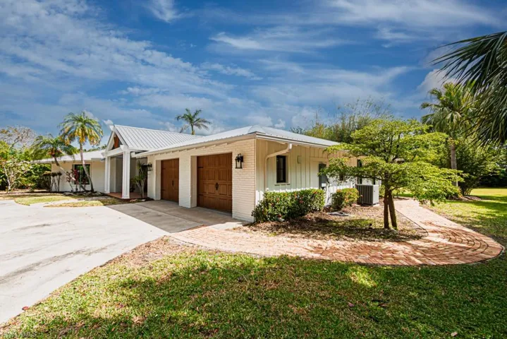 View of front of property with central air condition unit, a garage, driveway, metal roof, and brick siding