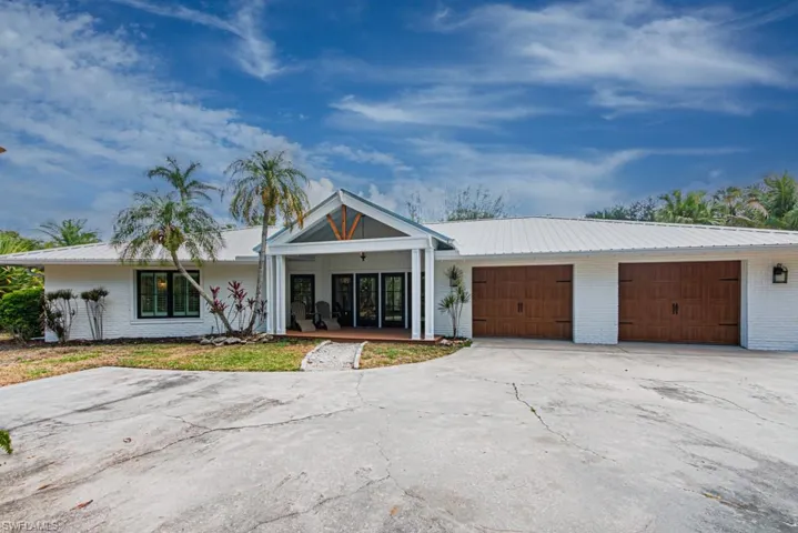 View of front of house featuring brick siding, a garage, metal roof, concrete driveway, and covered porch