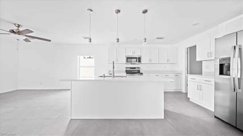 Kitchen with appliances with stainless steel finishes, white cabinetry, hanging light fixtures, light tile patterned floors, and a kitchen island with sink