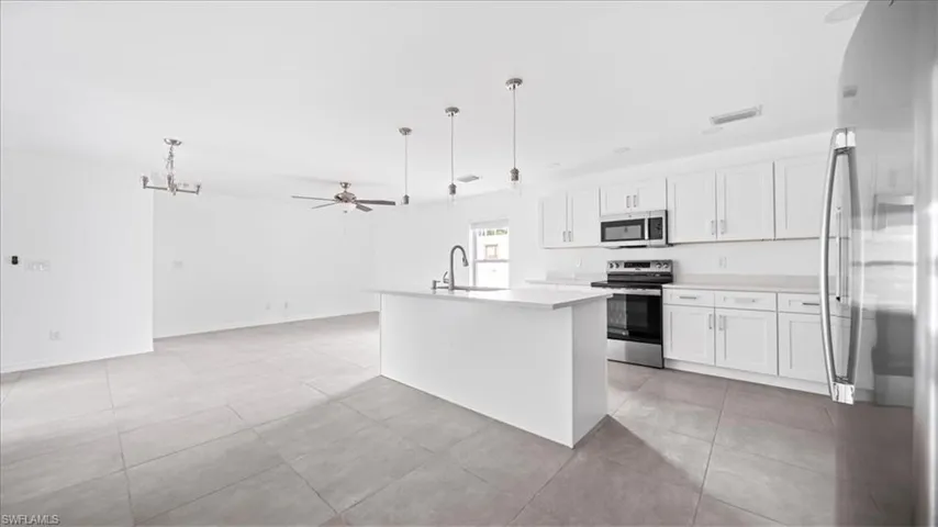 Kitchen with a ceiling fan, appliances with stainless steel finishes, pendant lighting, an island with sink, and white cabinets