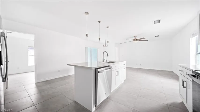 Kitchen with white cabinets, appliances with stainless steel finishes, pendant lighting, a ceiling fan, and a kitchen island with sink