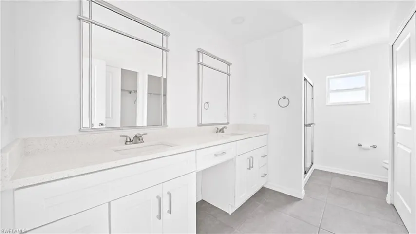 Full bath featuring double vanity, a stall shower, light tile patterned flooring, and a closet