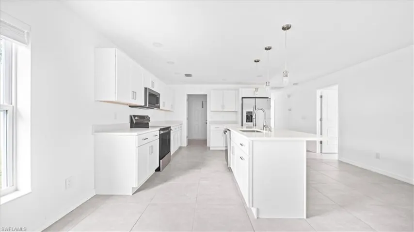 Kitchen with appliances with stainless steel finishes, white cabinets, decorative light fixtures, a kitchen island with sink, and light tile patterned flooring