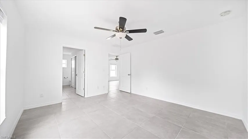 Unfurnished bedroom with ceiling fan, light tile patterned flooring, and connected bathroom