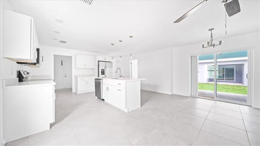 Kitchen featuring white cabinets, decorative light fixtures, a kitchen island with sink, a ceiling fan, and appliances with stainless steel finishes