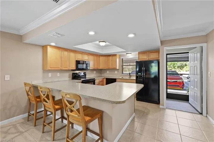Kitchen featuring black appliances, kitchen peninsula, ornamental molding, and a breakfast bar