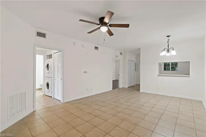 Empty room featuring light tile patterned floors, stacked washer and clothes dryer, and ceiling fan with notable chandelier