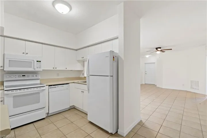 Kitchen with white appliances, ceiling fan, light tile patterned flooring, and white cabinets