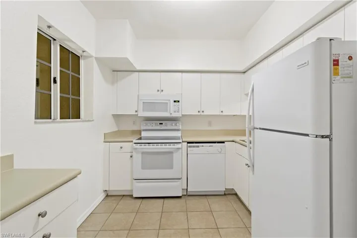 Kitchen featuring white cabinets, light tile patterned flooring, and white appliances