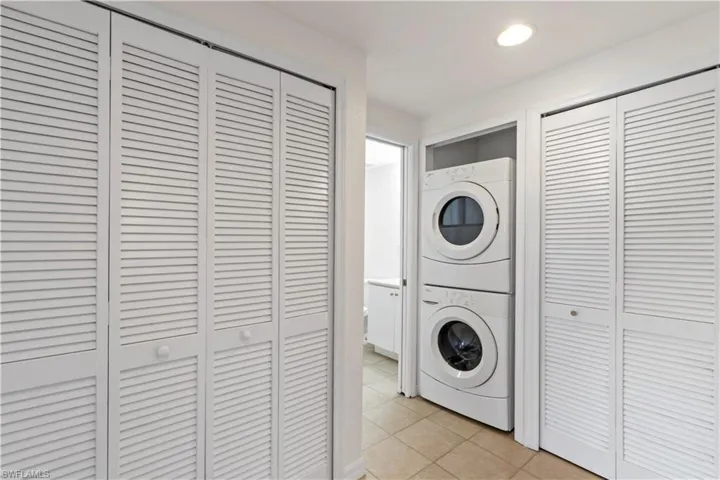 Clothes washing area with stacked washer and clothes dryer and light tile patterned floors