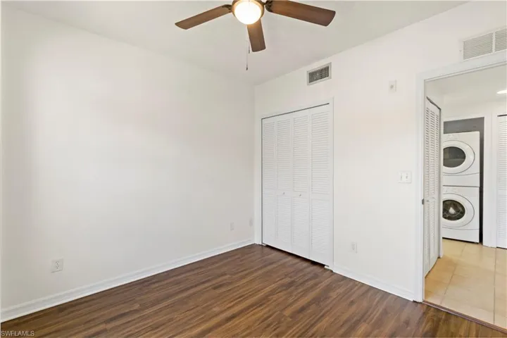 Unfurnished bedroom featuring hardwood / wood-style flooring, stacked washer / drying machine, and ceiling fan