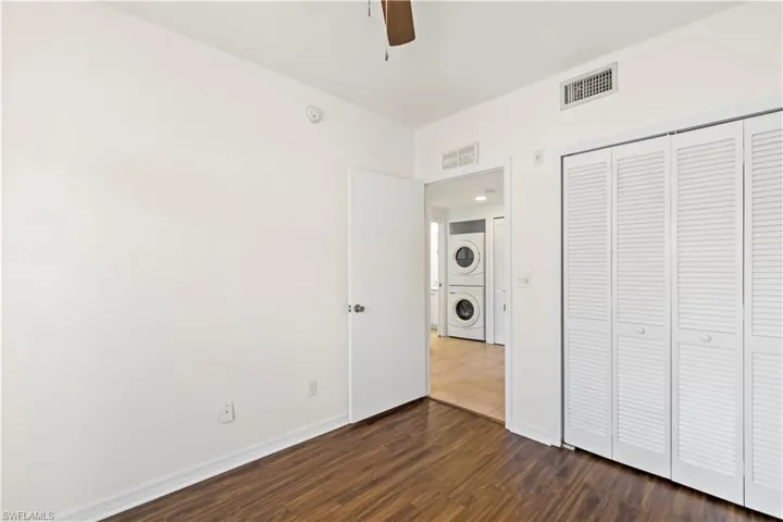 Unfurnished bedroom featuring a closet, ceiling fan, stacked washer / drying machine, and hardwood / wood-style flooring