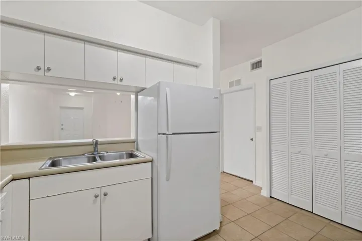 Kitchen with light tile patterned flooring, sink, white fridge, and white cabinets