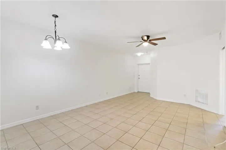 Tiled empty room featuring ceiling fan with notable chandelier