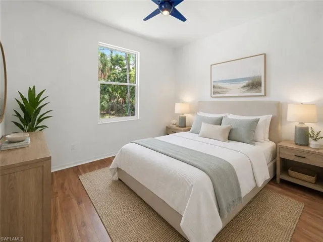 Bright bedroom featuring wood-finish flooring, a contemporary ceiling fan, and a large window overlooking natural foliage
