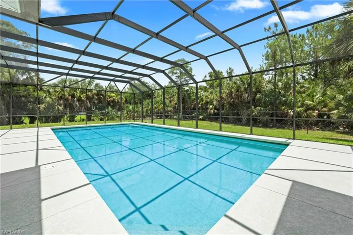 Screened outdoor swimming pool featuring a rectangular shape, light blue interior finish, and a substantial concrete pool deck