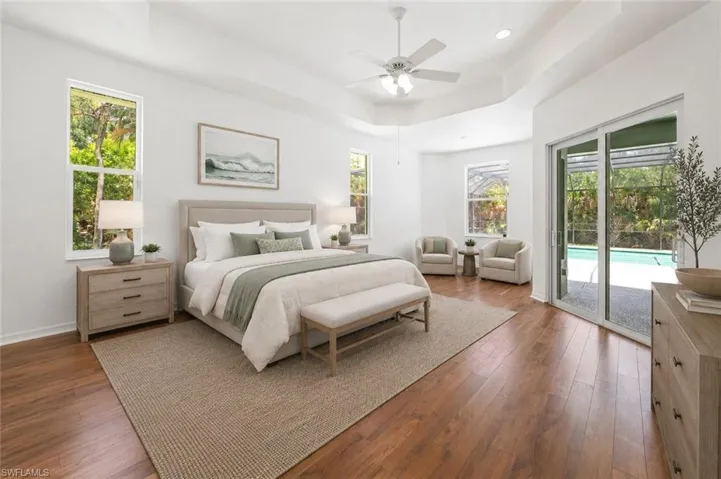 Spacious room featuring wood-finish flooring, a tray ceiling with a ceiling fan, and multiple windows providing natural light
