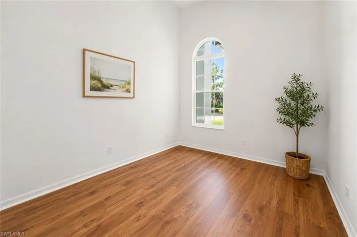 Room with an arched window, wood-finish flooring, white baseboards, and bright white walls
