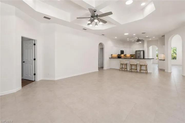 Spacious interior featuring neutral tile flooring, a tray ceiling with recessed lighting and a ceiling fan, and a kitchen with white cabinetry, black countertops, and stainless steel appliances