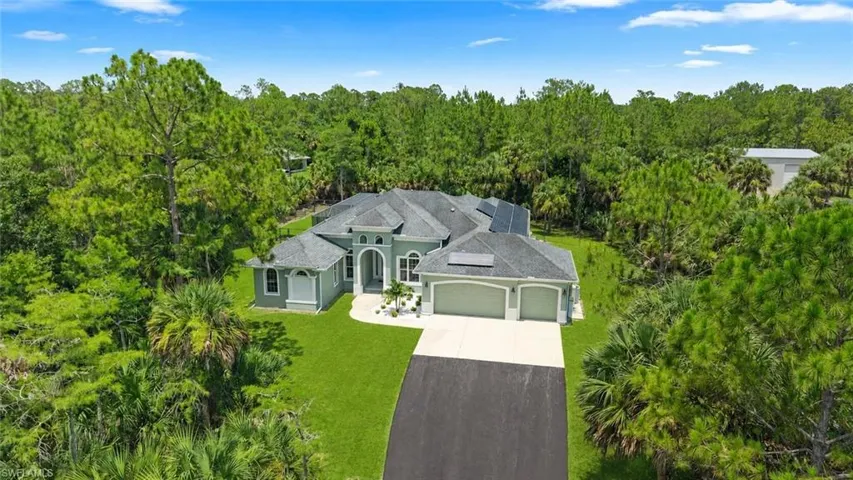 Contemporary residence featuring a light green exterior, a dark shingle roof, and a paved driveway leading to a two-car garage