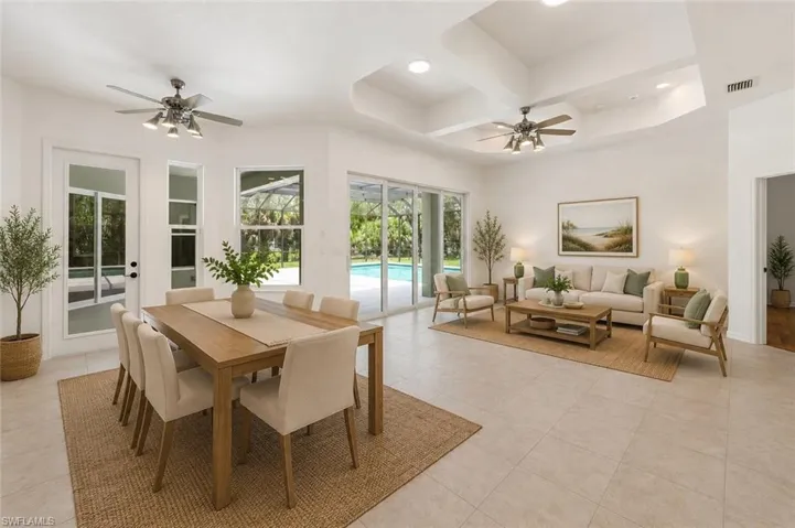 Bright open-concept living area featuring tile flooring, tray ceilings, recessed lighting, and direct access to the outdoor pool area via sliding glass doors