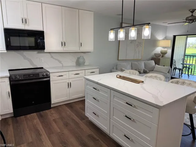 Kitchen with electric range, a breakfast bar, black microwave, white cabinets, and open floor plan