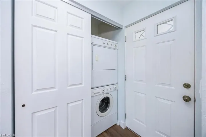 Washroom with stacked washer and clothes dryer and dark wood-style floors
